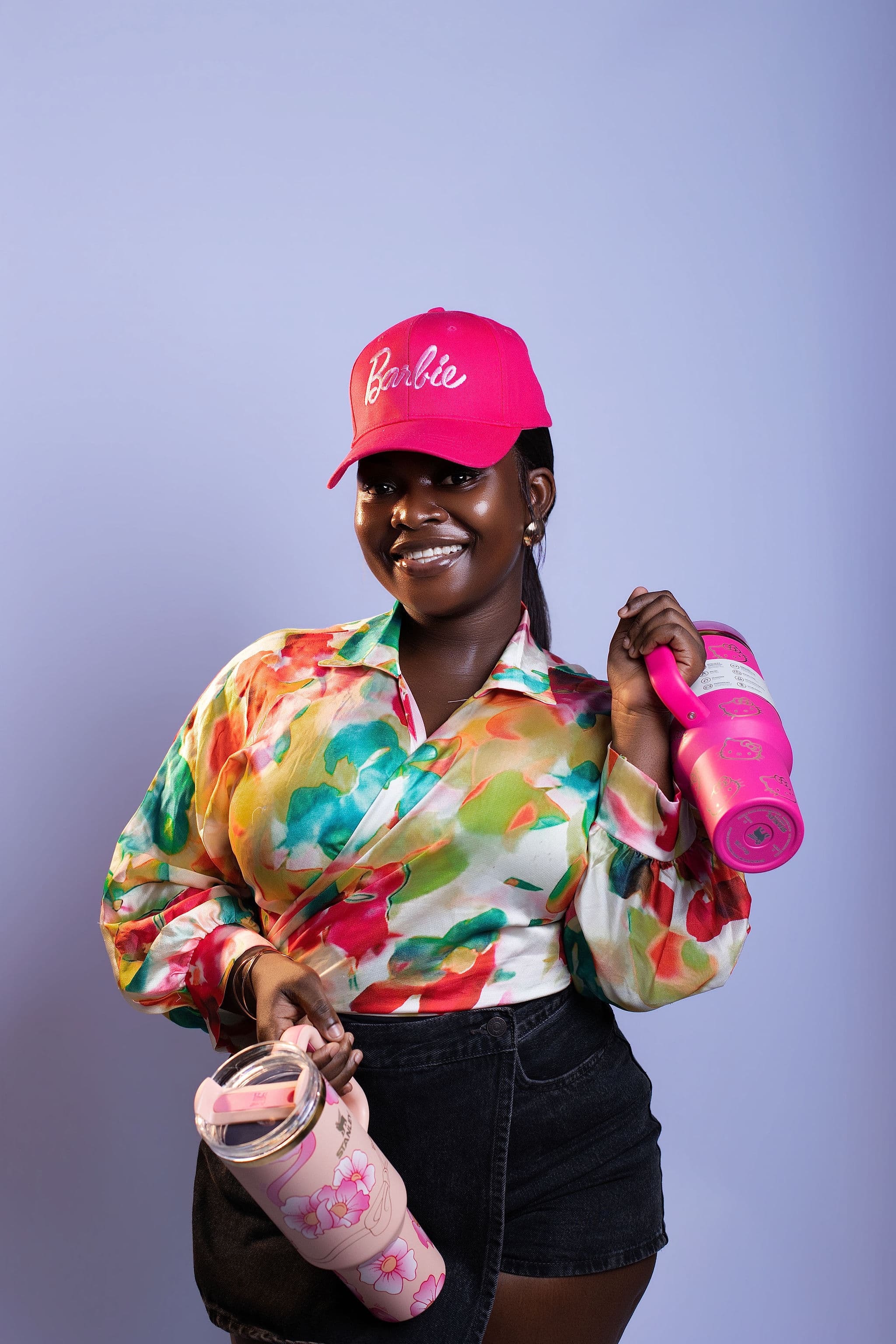 A lady smiling wearing a barbie cap and holding tumblers
